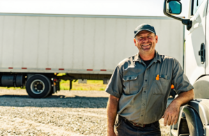 Commercial truck driver standing beside his semi-truck in bright daylight