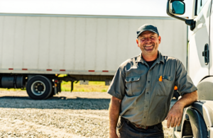 Commercial truck driver standing beside his semi-truck in bright daylight