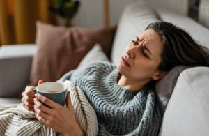 Woman resting on a couch with a warm mug while recovering from a stomach bug in Vancleave MS