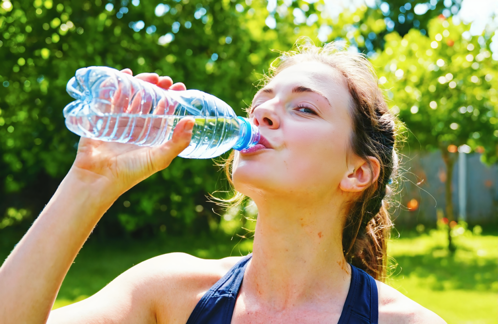 Young woman drinking from a water bottle outdoors in a sunny backyard on a hot Gulf Coast day