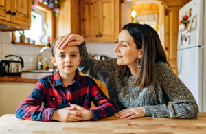 Mother checking her young daughter's forehead for a fever at a home kitchen table