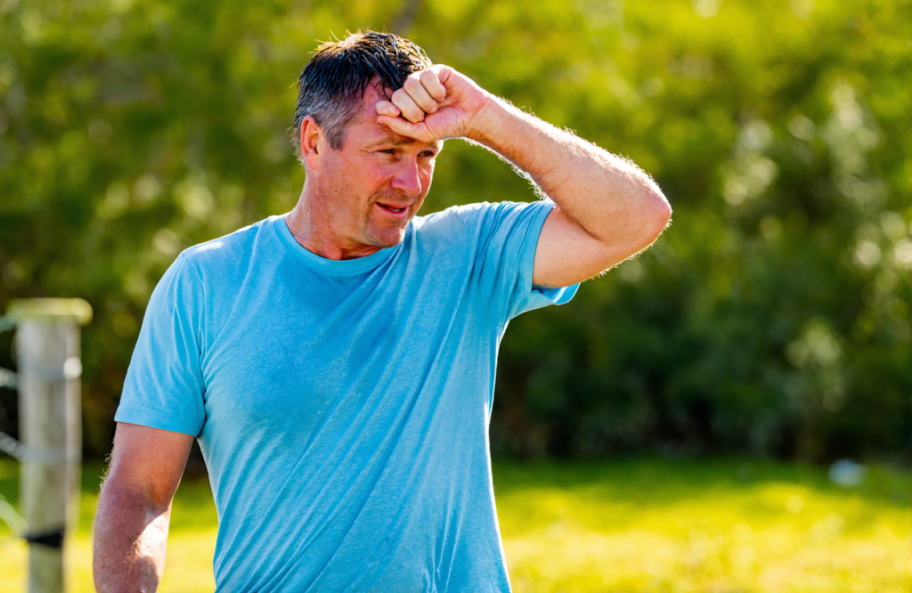 Man wiping sweat on a hot Gulf Coast day, a common reason people seek IV hydration therapy