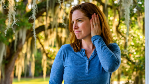 Woman on a back porch pressing her palm over a plugged, muffled ear, a common reason people look for ear cleaning