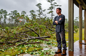 Man on a wet porch looking over downed pine branches, figuring out what to do after a hurricane in Jackson County, MS